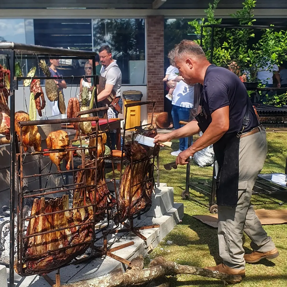 Assador cuidando de costelas, frangos e carnes no fogo de chão durante um evento ao ar livre